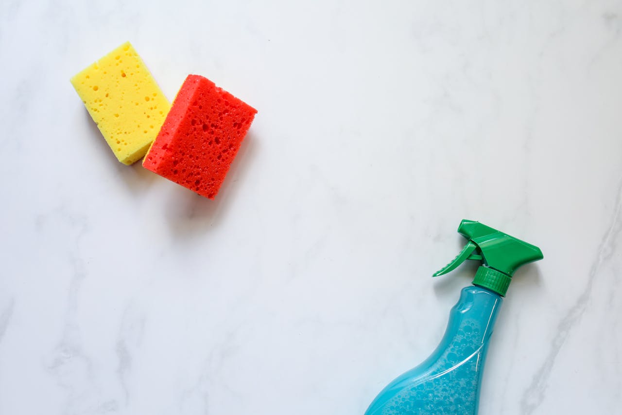 about-01 Red and yellow sponges with a blue spray bottle on a marble background, offering cleaning themes.