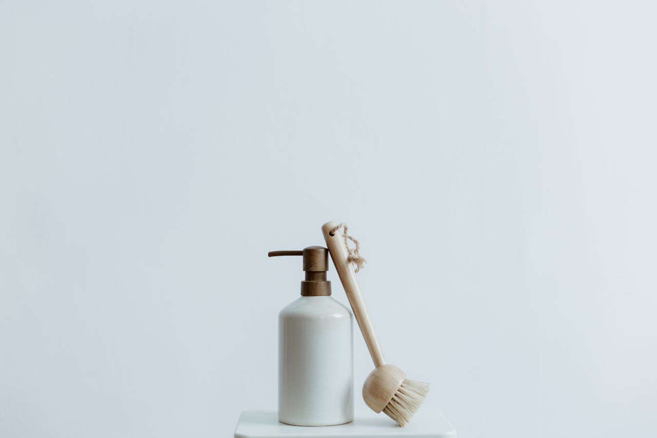services-01 A minimalist soap dispenser and wooden brush set against a plain white background.